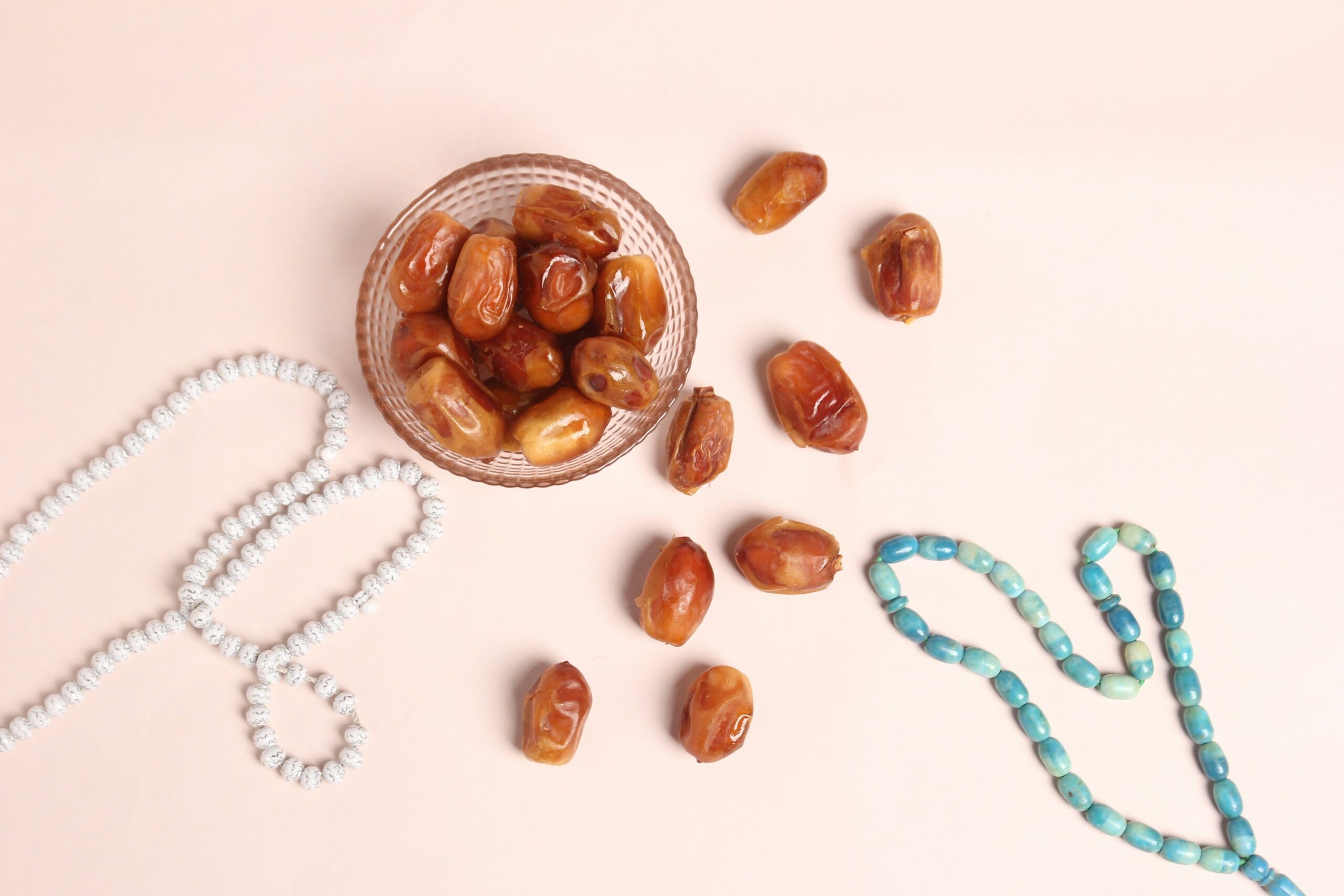Beautiful Dates in cup with prayer Beads photography on light pink background.